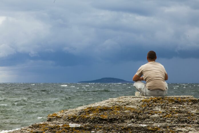 en man som mediterar på en sten med havet i bakgrunden